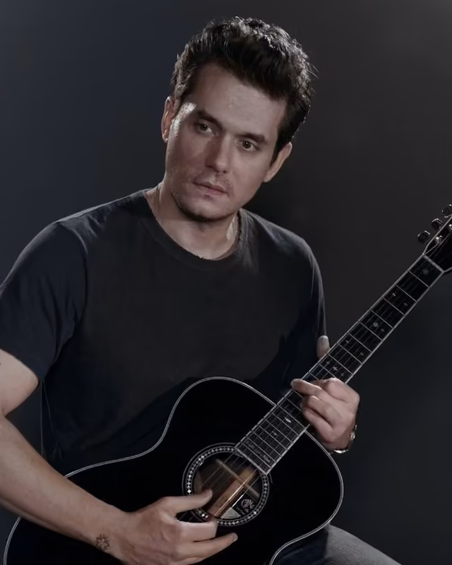 A colour photograph of a man singing into a microphone while playing an electric guitar on stage, lit in blue stage light.