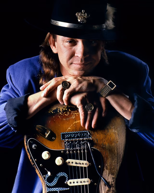 A black-and-white photograph of a man wearing a wide-brimmed hat, shown from the chest up against a plain studio background.
