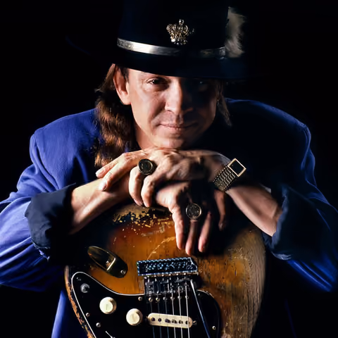 A black-and-white photograph of a man wearing a wide-brimmed hat, shown from the chest up against a plain studio background.