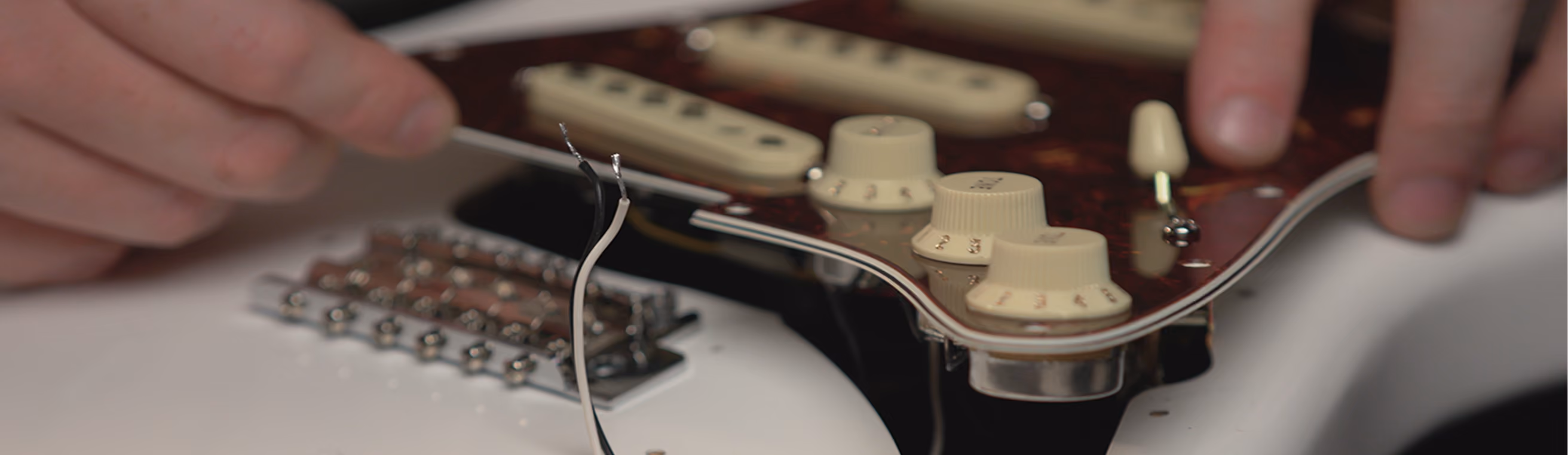 Inside a guitar's control cavity, showing potentiometers wired together with coloured hookup wire — the passive circuit this week studies.