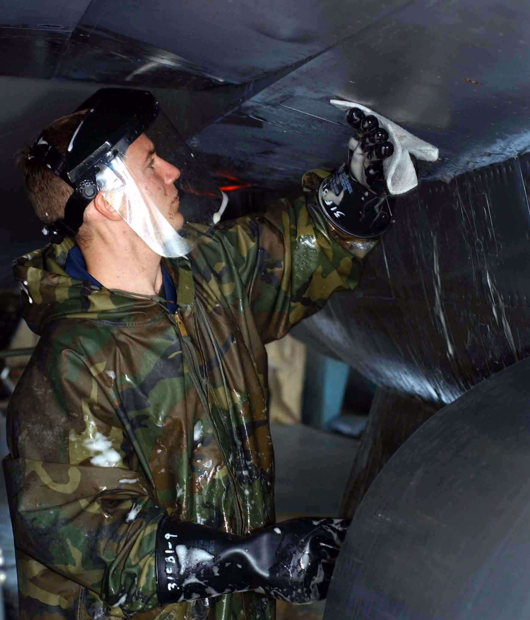 A crew chief in protective gear scrubbing down an F-16, close beside its fuselage