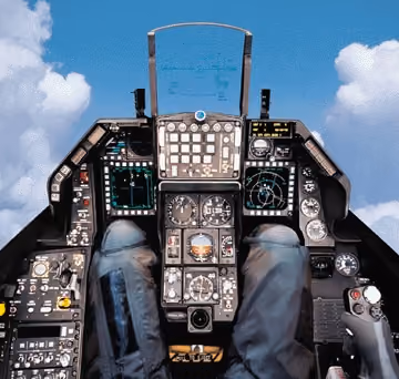 An F-16 cockpit instrument panel, gauges and indexer lights visible under the canopy rail