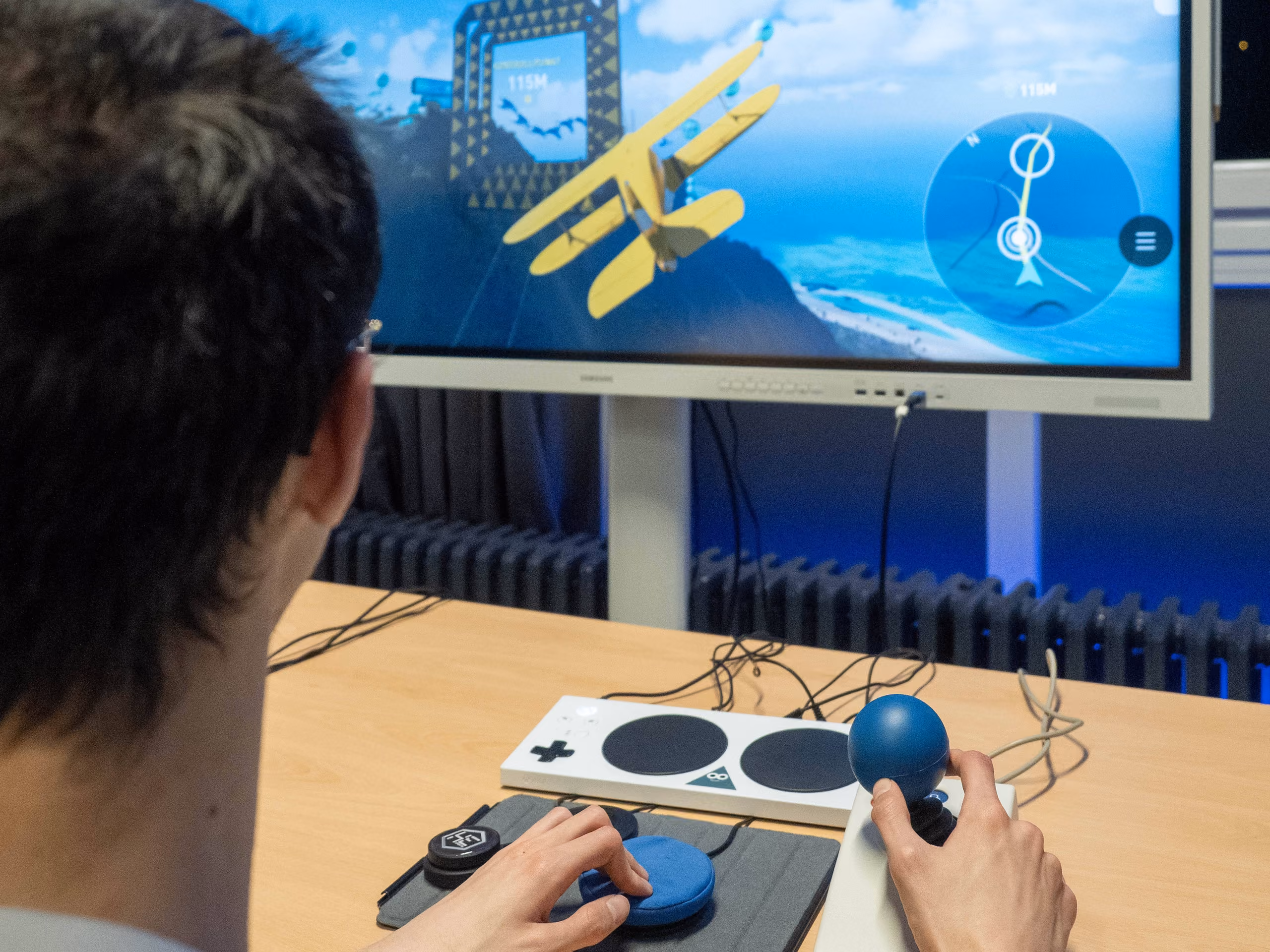 A person using an Xbox Adaptive Controller and a large joystick to fly a biplane in a flight simulator