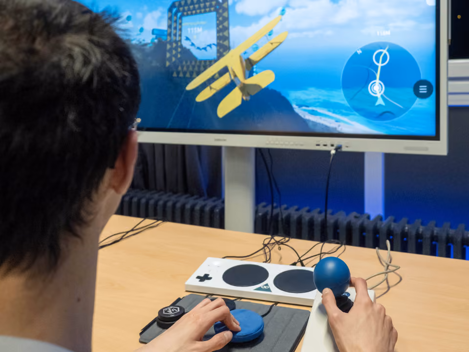 A person using an Xbox Adaptive Controller and a large joystick to fly a biplane in a flight simulator