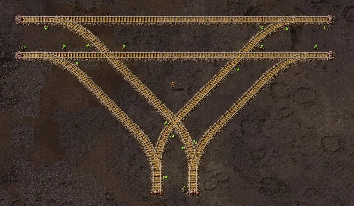 A wiki screenshot of two double-track main lines each narrowing through curved crossover track into a single shared line, forming two parallel merge points side by side, each guarded by its own signals