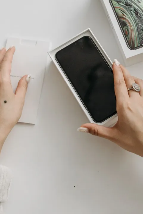 A person's hands lifting a smartphone out of its retail box on a table, mid-unboxing.