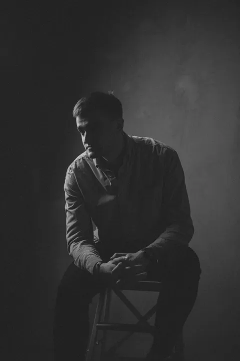 A moody black-and-white studio portrait of a man in quiet contemplation, dramatic side lighting.