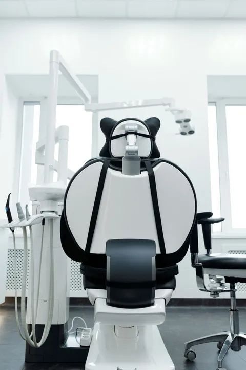 A bright, empty modern dental clinic room with a reclined dental chair and overhead exam light, no patients or staff present.