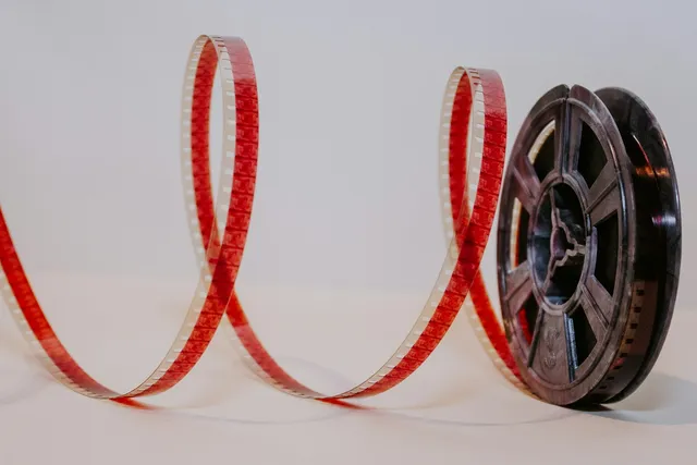 A coiled strip of film unspooling from a reel against a plain backdrop.