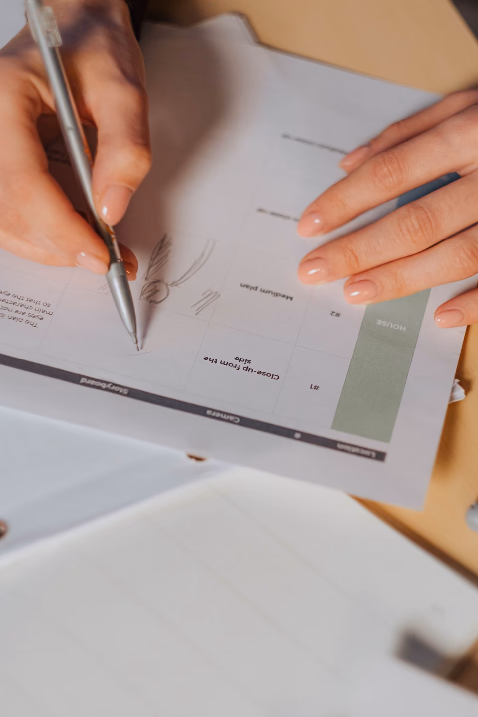 Close-up of a woman's hands sketching notes onto a printed storyboard template, its "Storyboard / Camera" column headers visible