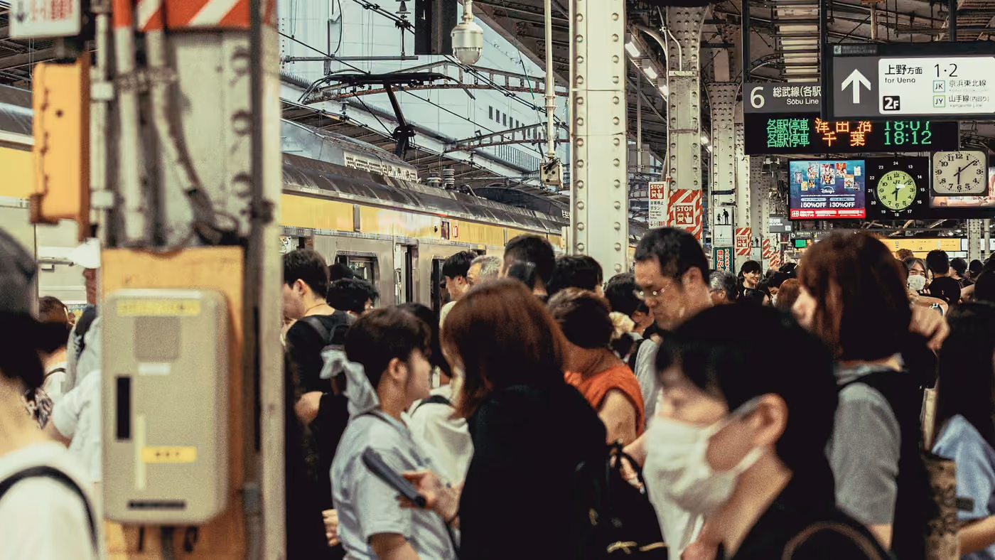 A dense crowd waiting the length of a train platform under signage