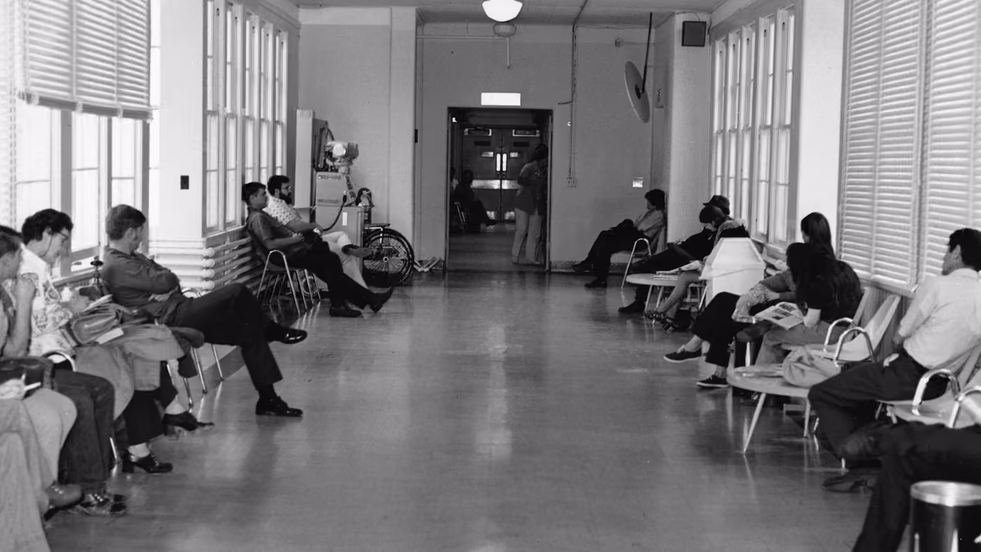 People sitting along both sides of a hallway lined with chairs, waiting