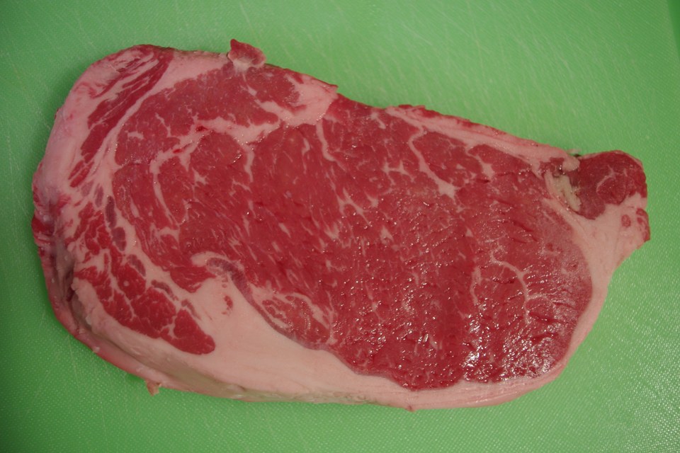 A raw beef steak on a cutting board, its cut surface a bright cherry-red where it has been freshly exposed to air