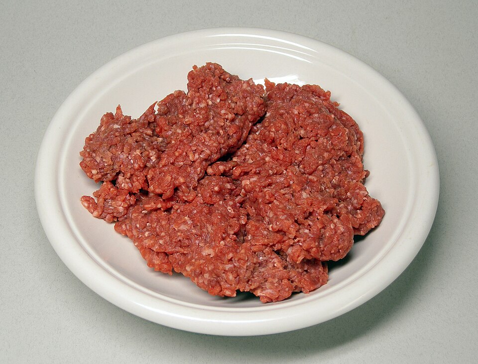 Ground beef heaped on a plate, its surface broken into many small fragments rather than one intact face