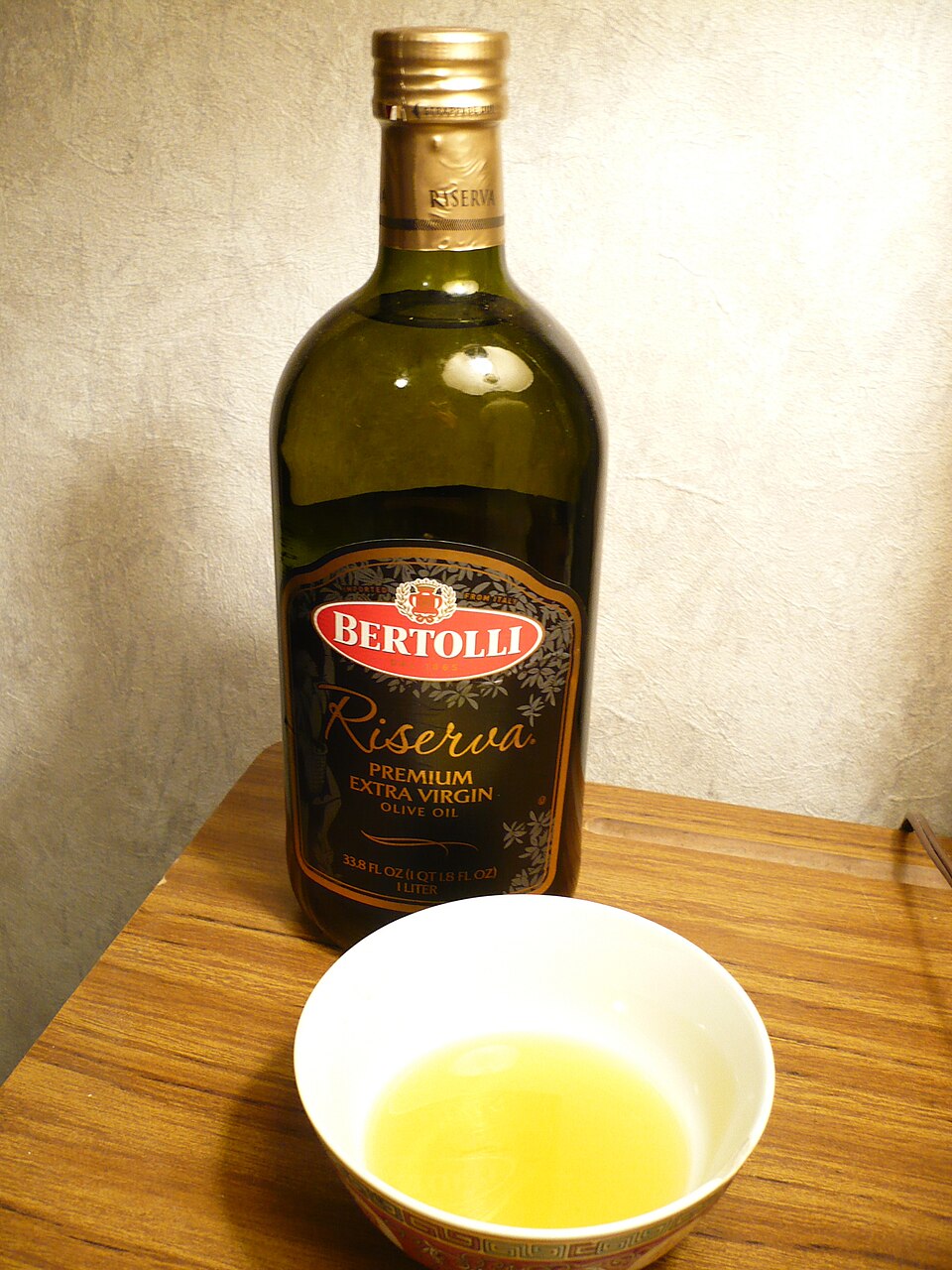A bottle of olive oil standing beside a small bowl of poured oil