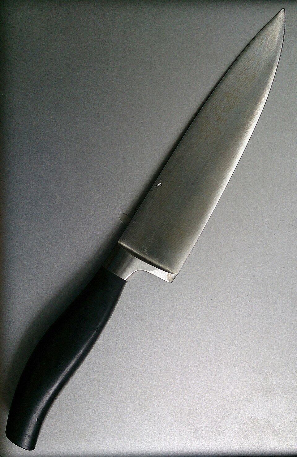 A chef's knife, blade and handle in one piece, resting on a plain surface