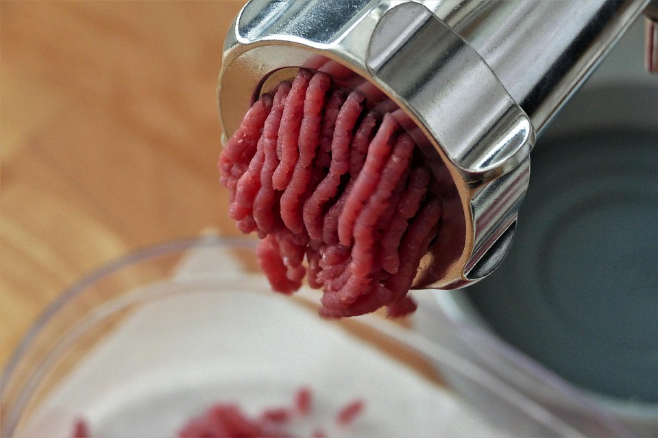 Raw ground beef extruding from a meat grinder, showing how grinding distributes material from across the whole piece rather than leaving it on a single outer surface