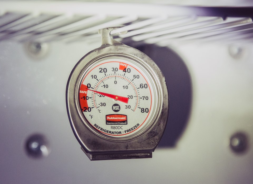 A dial refrigerator and freezer thermometer marked with safe temperature zones, hanging inside a fridge