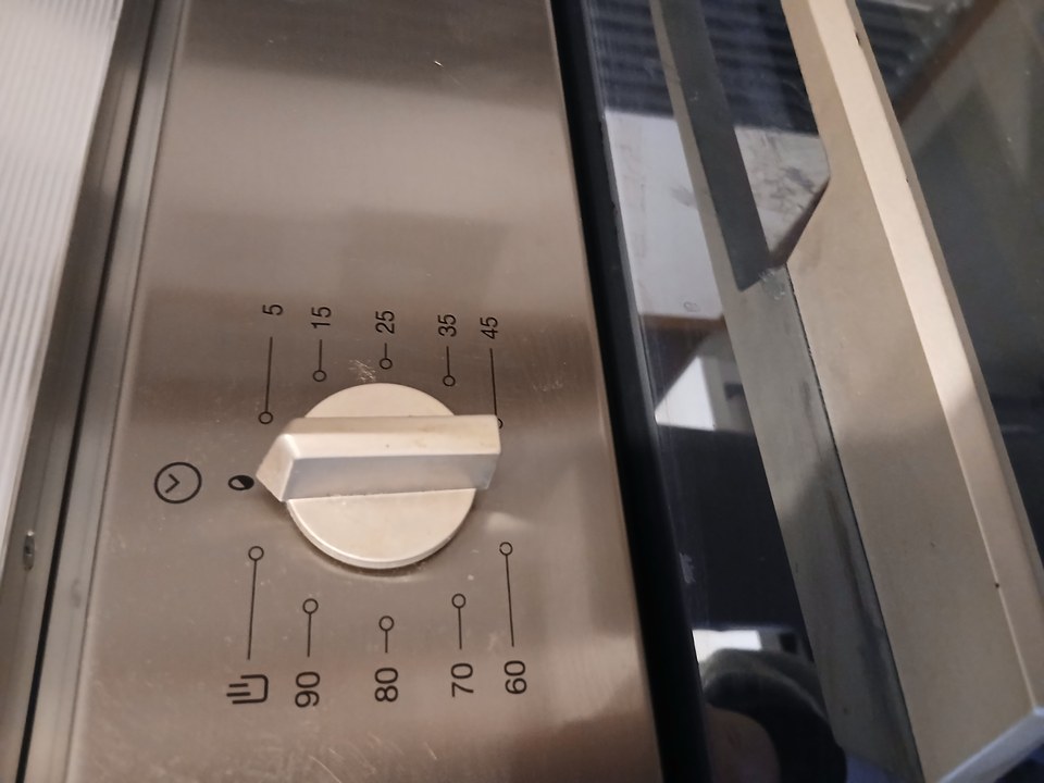 Close-up of a mechanical kitchen timer dial mounted on an oven, marked in minutes from 5 to 90