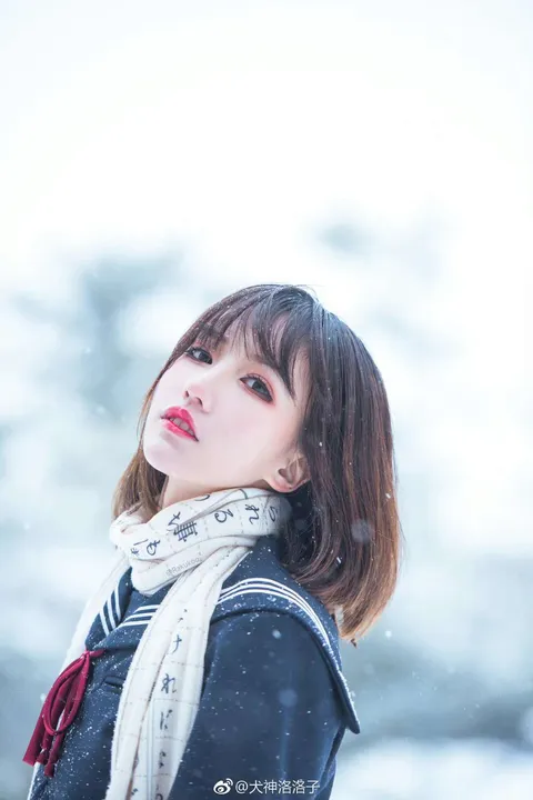 Portrait of Kiroro in falling snow, wearing a dark sailor-style coat and light scarf.