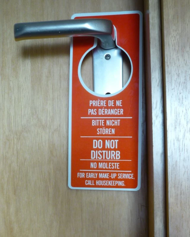 A red hotel door hanger says “Do not disturb” in French, German, English and Spanish. A smaller line gives instructions for requesting housekeeping.