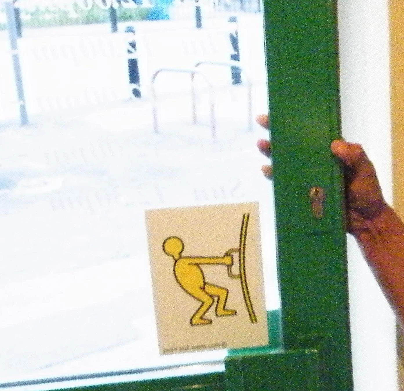 A photograph of a hand pulling a green door beside a yellow pictogram showing a person pulling a door towards them.