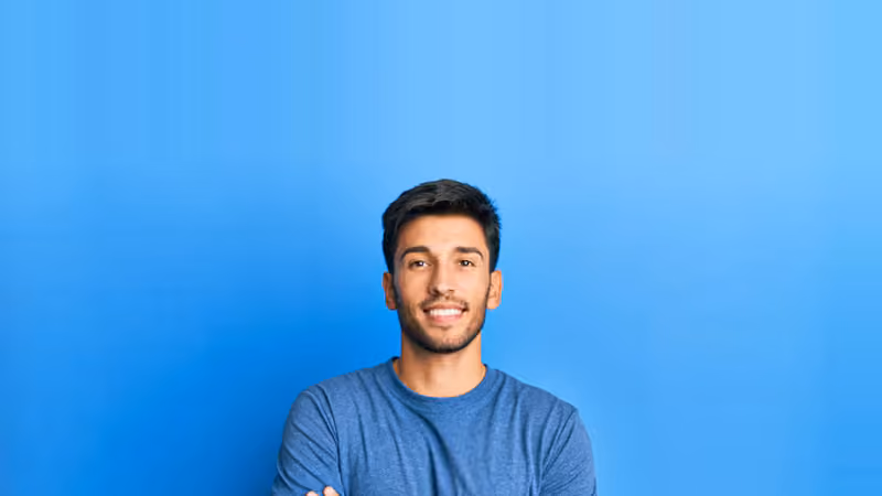 A portrait of a person facing the viewer, arms crossed and smiling, against a plain blue background