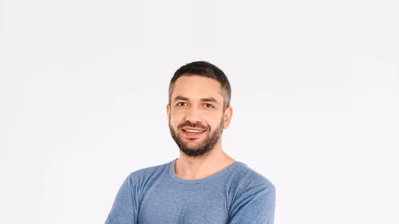 A portrait of a person in three-quarter view, arms crossed and smiling, against a plain white background