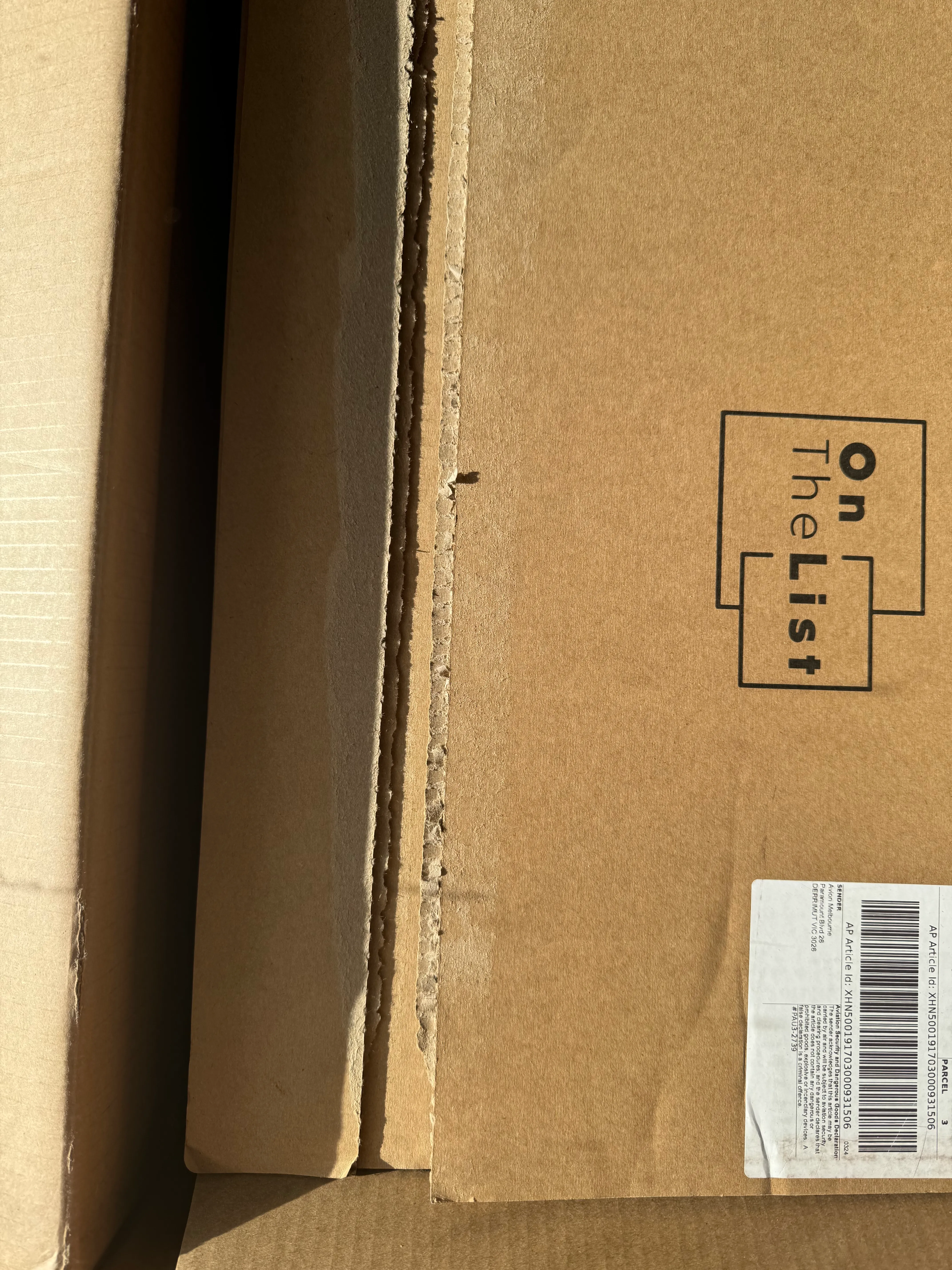 Close-up of an OnTheList shipping box showing the printed Aviation Security and Dangerous Goods Declaration label, with a torn packing-tape edge alongside it
