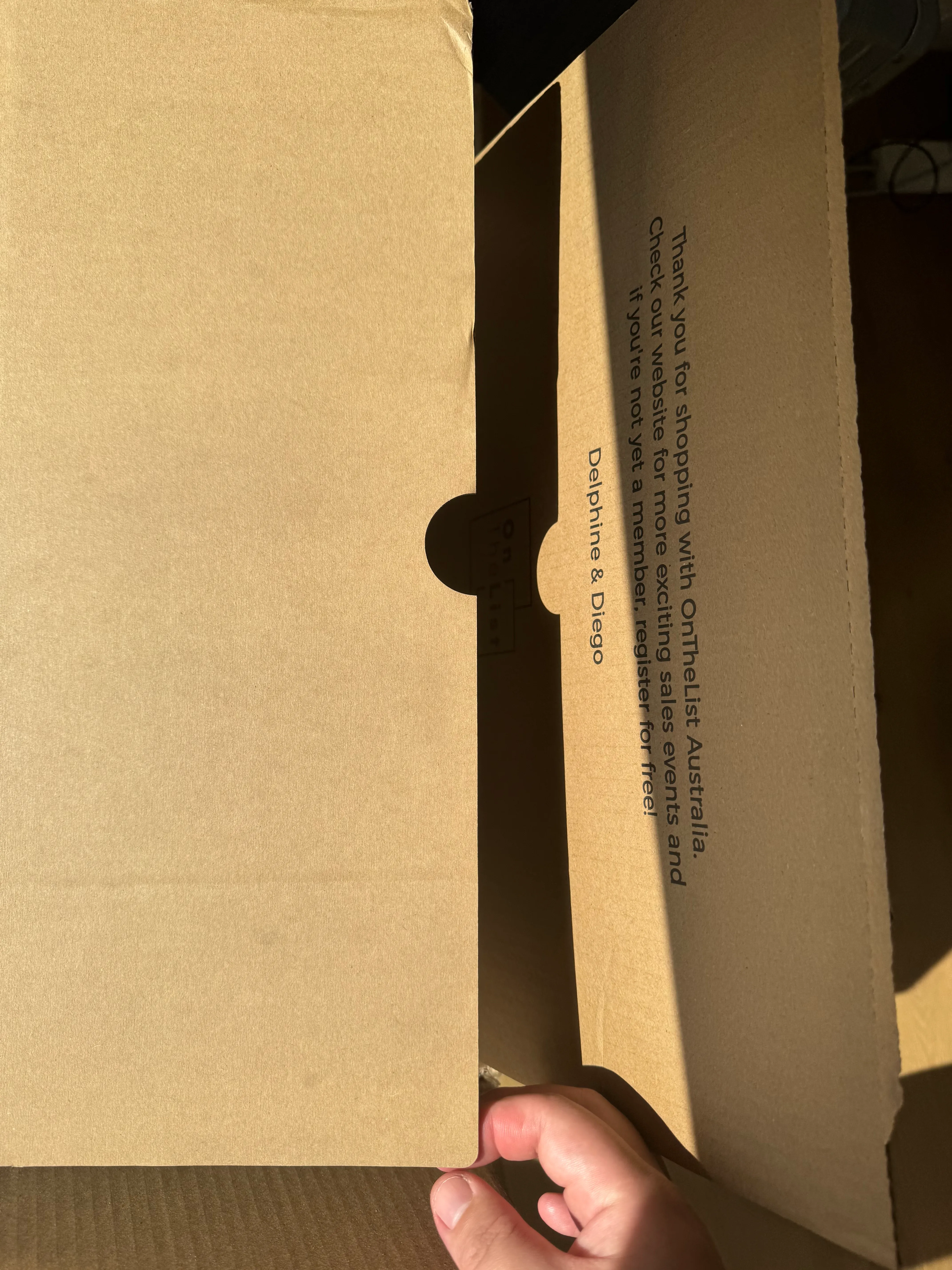 The inside of an OnTheList box lid, printed with a thank-you message, and a hand opening the box along its moulded perforated tear-strip