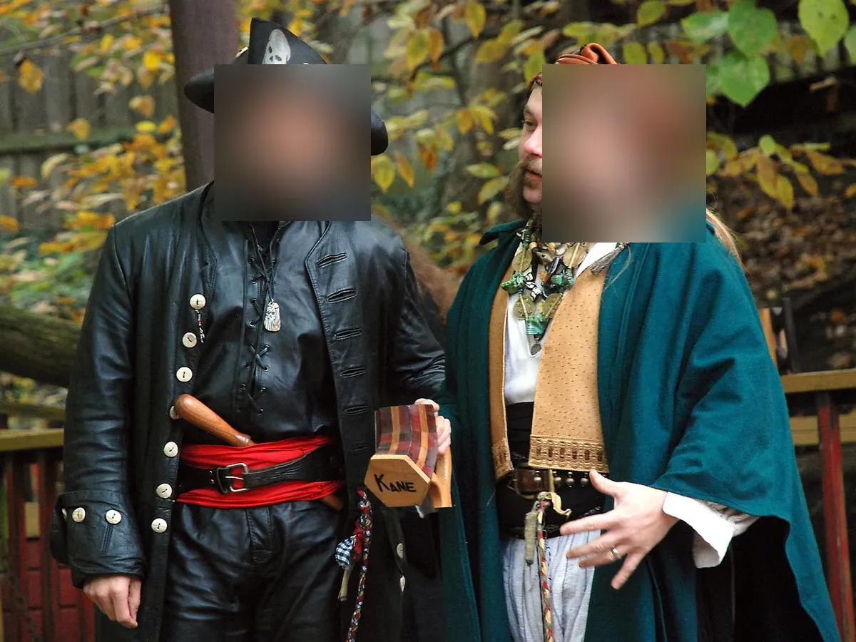Two people in full pirate costume, faces obscured, at an outdoor Renaissance fair, one wearing a tricorne hat and the other a teal cloak with layered necklaces.